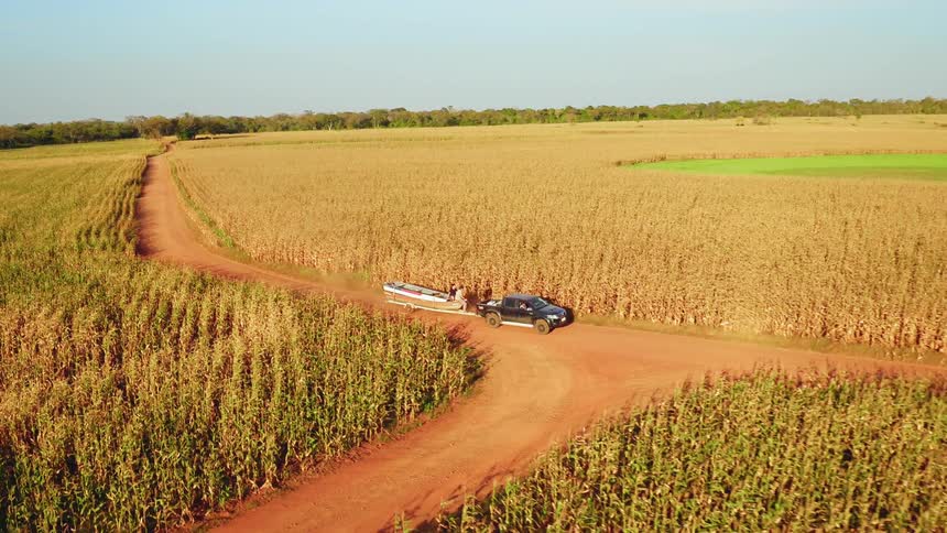 Truck tows a trailer on a dirt path between the fields