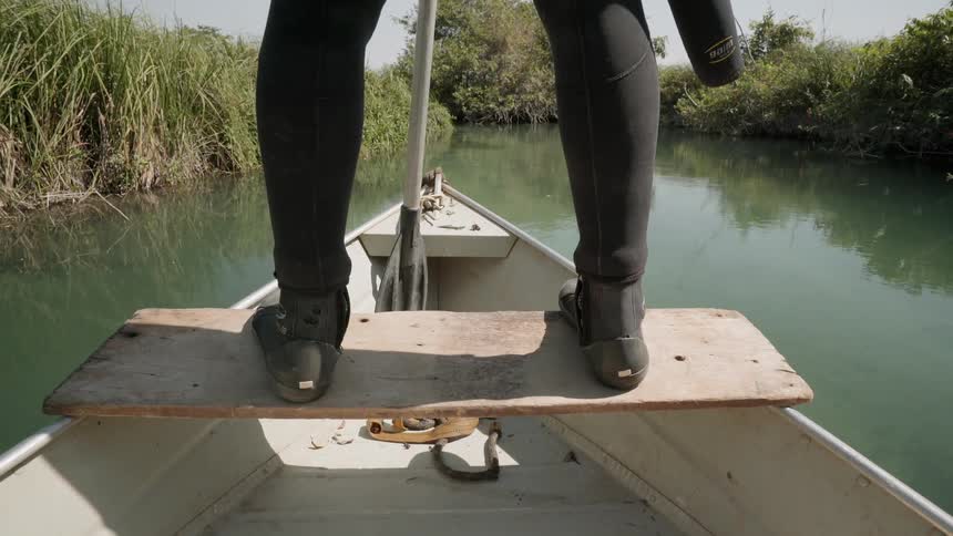 Person stands at the edge of a boat going down a small river