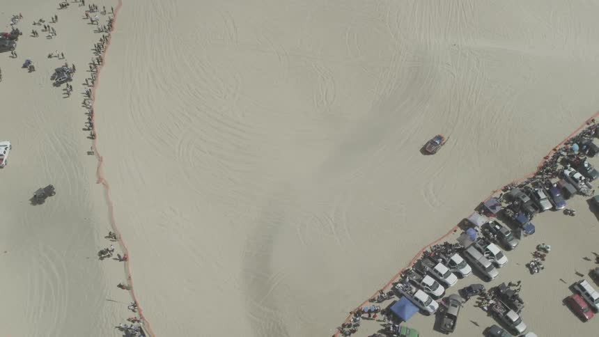 A vehicle drives through desert sand with many others parked nearby