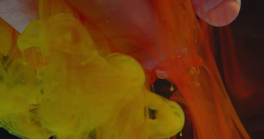 Yellow and red dye swirl around a woman's hand