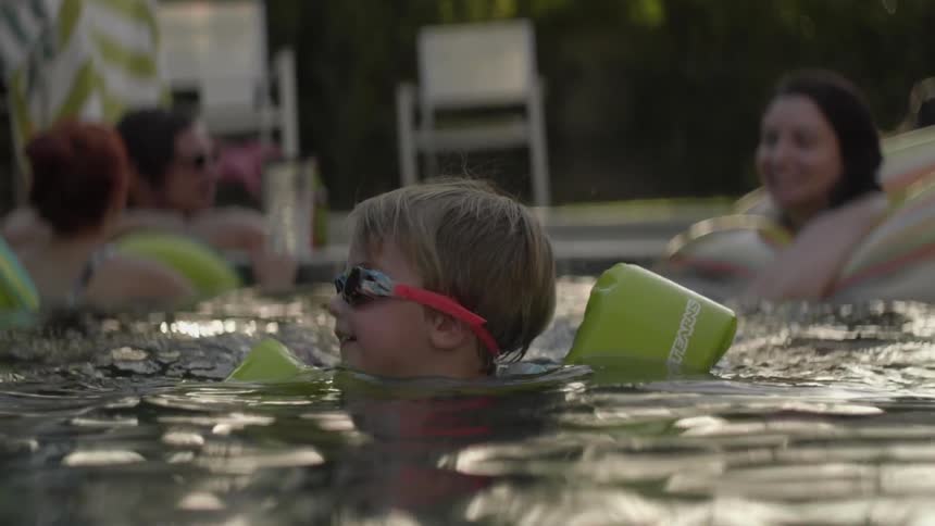 A young boy floats and splashes in a swimming pool