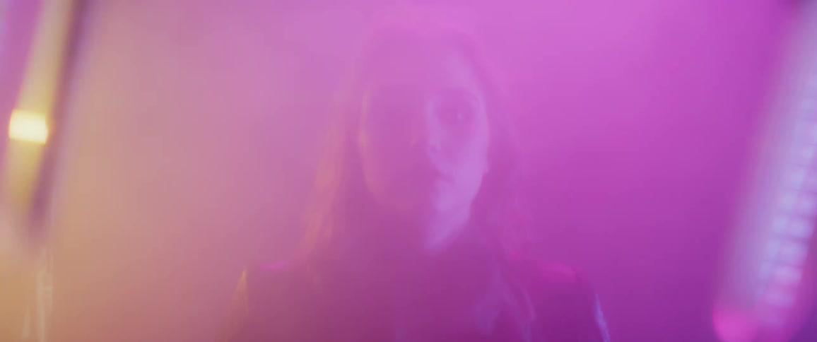 A woman stands in a hazy room with strobing colored lights
