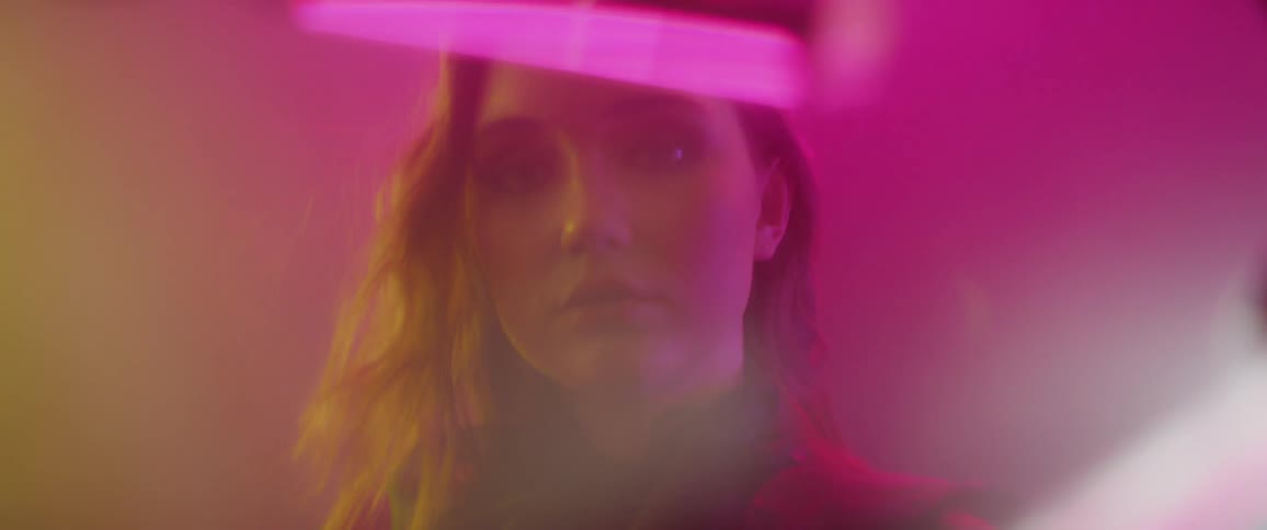 A woman stands in a foggy room with colorful lights