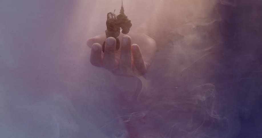 Dark liquid drops into a still hand in the water