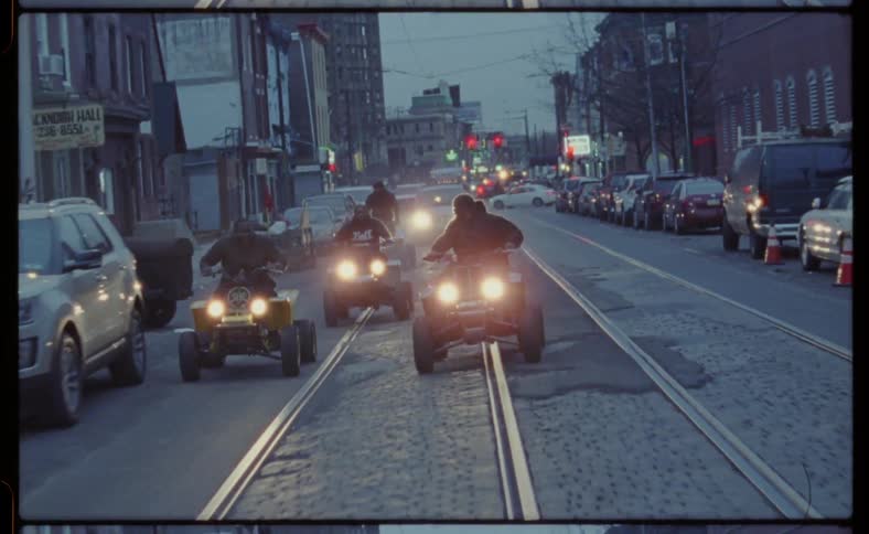 Men drive 4 wheelers on a city street and do tricks