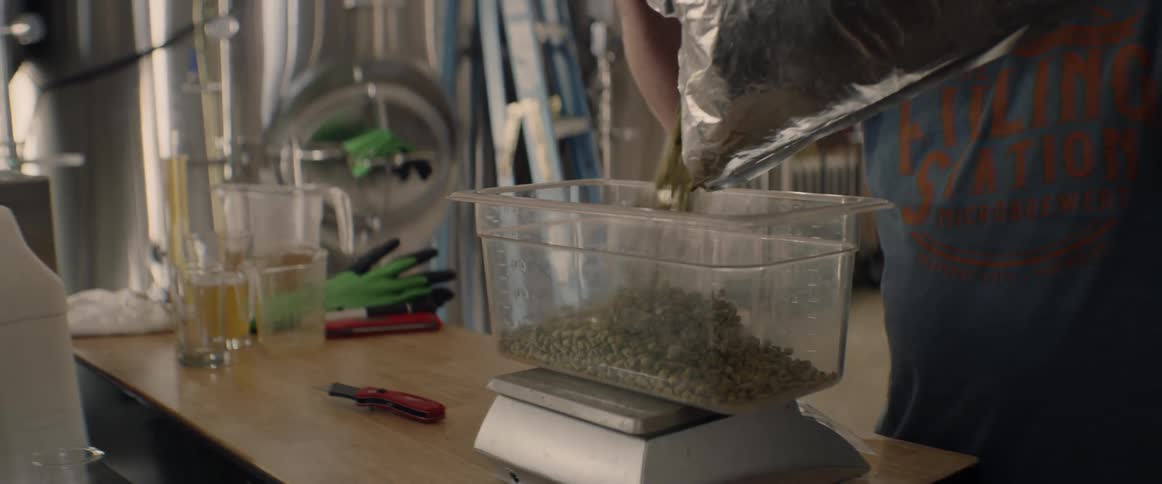 A man is pouring hops into a container on a scale inside in daylight