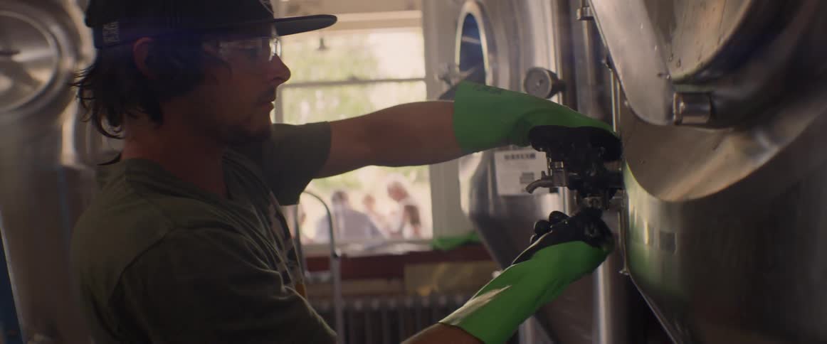 A man is securing a tap on a beer vat inside in daylight