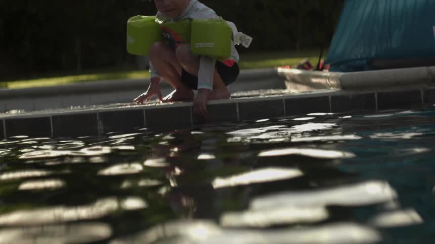 A child with floaties on touches the pool water