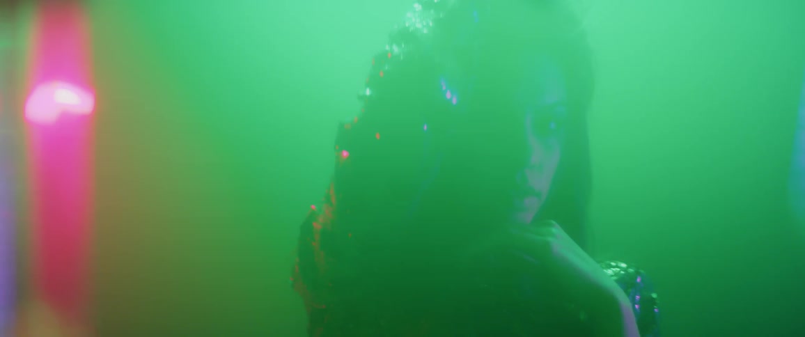 A woman dances and plays with her hair under colored lights