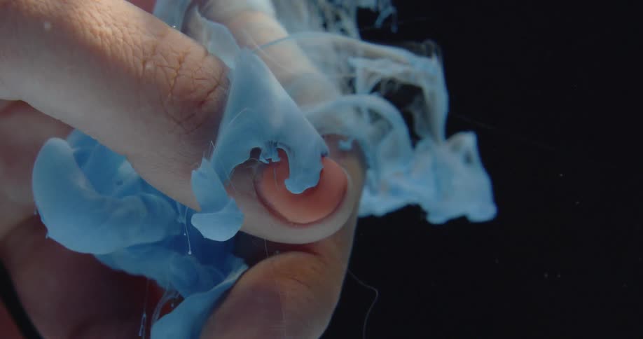 A cloud of paints flows around fingers under water