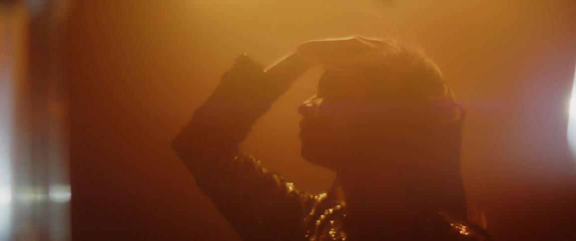 A woman pulls her hair back as the wind blows it and colored lights shine