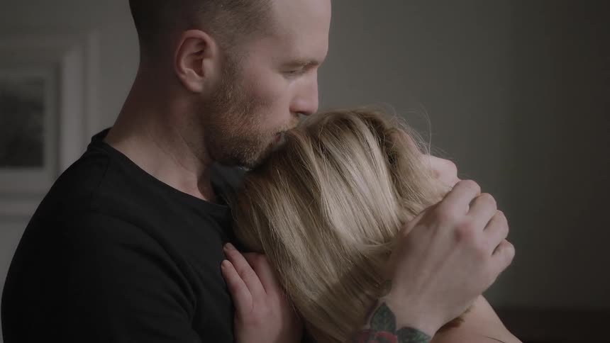 A man holds a woman in his arms and kisses the top of her head