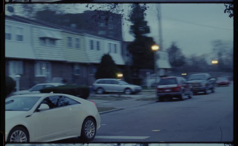 Vehicles drive down a busy city street in the evening