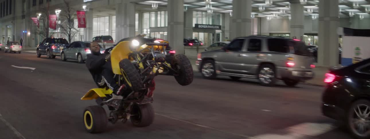 Two people ride on four wheelers down a city street at night