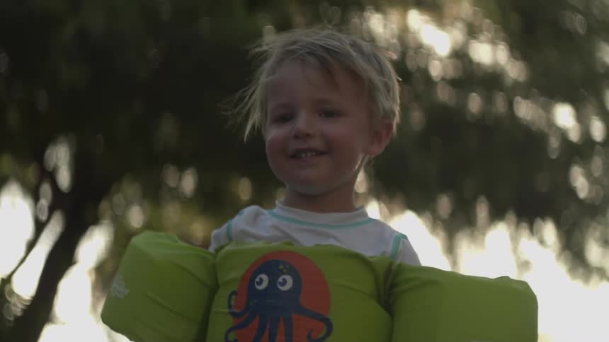 Smiling child standing in a yard wearing a flotation device