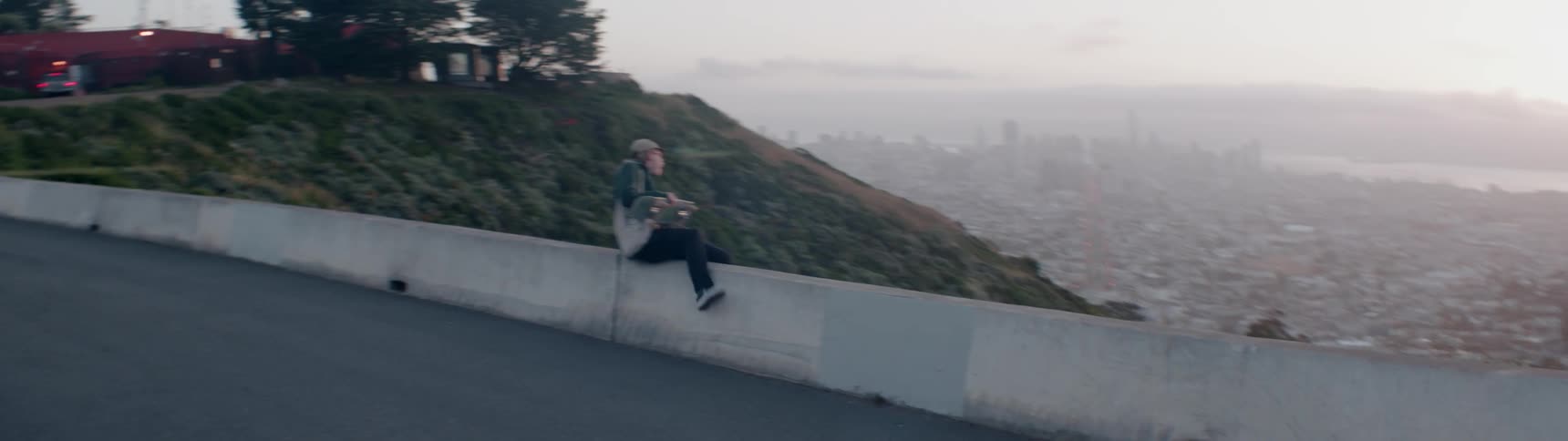 A skateboarder stops to look out from atop a mountain
