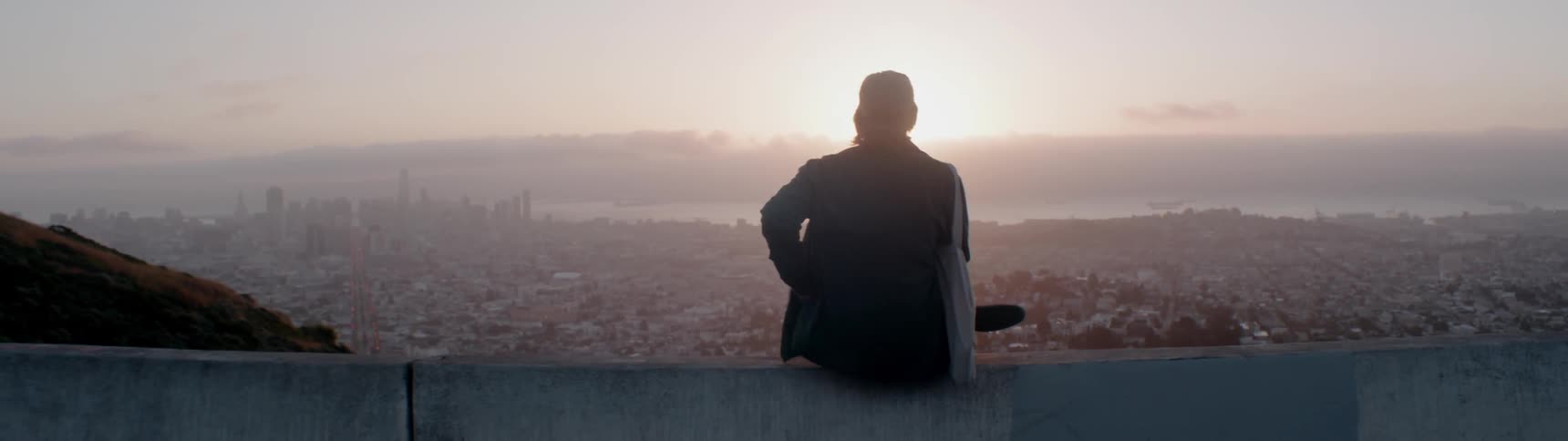 A skateboarder overlooks a cityscape at sunset