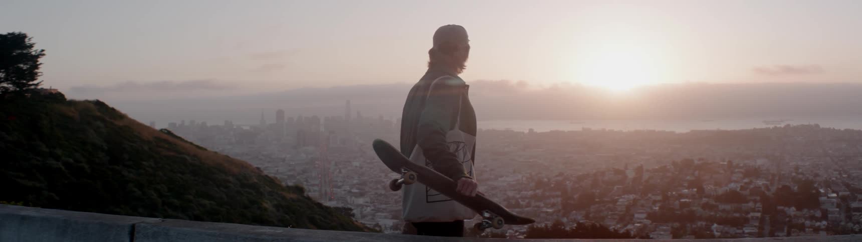 A skateboarder looks out from atop a mountain