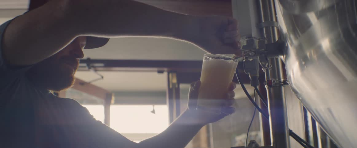 A man is drawing beer from a vat inside in daylight