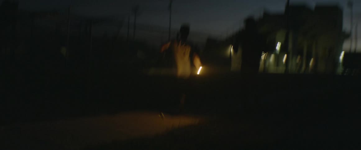 Boys carrying a flashlight run and climb over a chain link fence