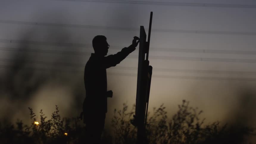 A man paints on a canvas outside at sunset