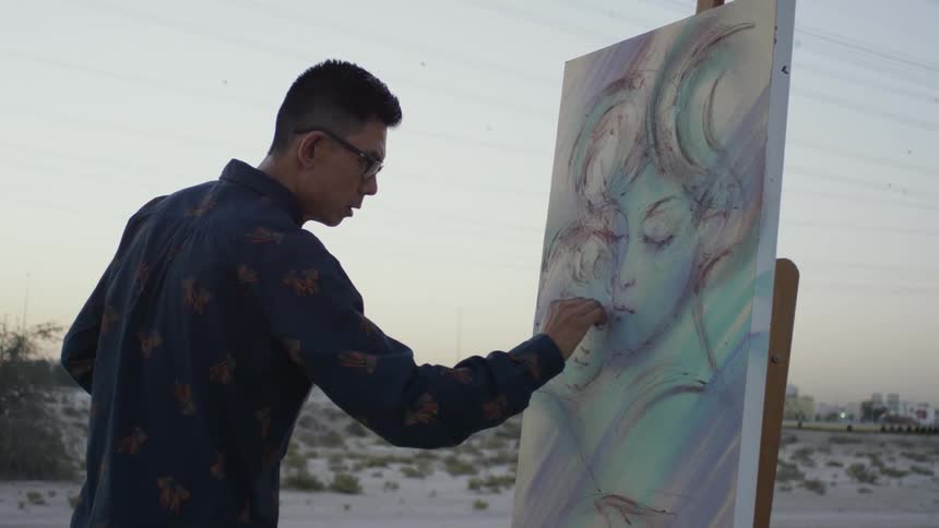 An artists is creating an artwork on canvas outside at dusk