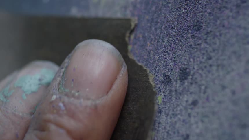 A man is sanding the surface of a canvas painting