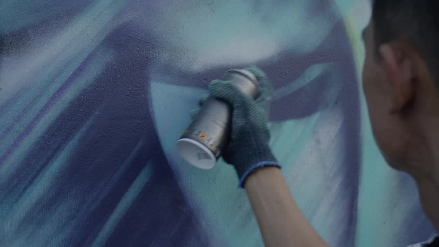 A man wearing a glove uses spray paint on a wall mural