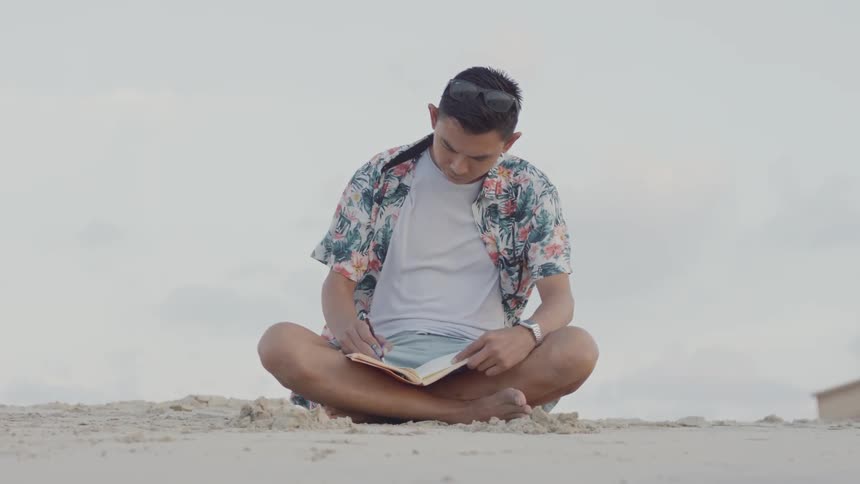 A man is sitting on the beach on a windy day drawing in a sketchbook