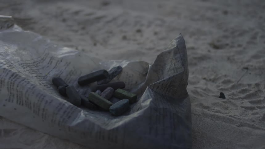 Pieces of colored chalk sit on top of a plastic bag on the sand
