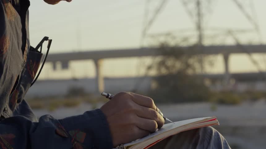 A man is sketching in a notebook outside at dusk