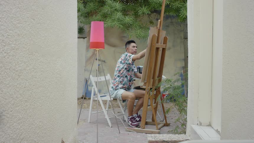 Man sits as he draws on a canvas sitting on an easel