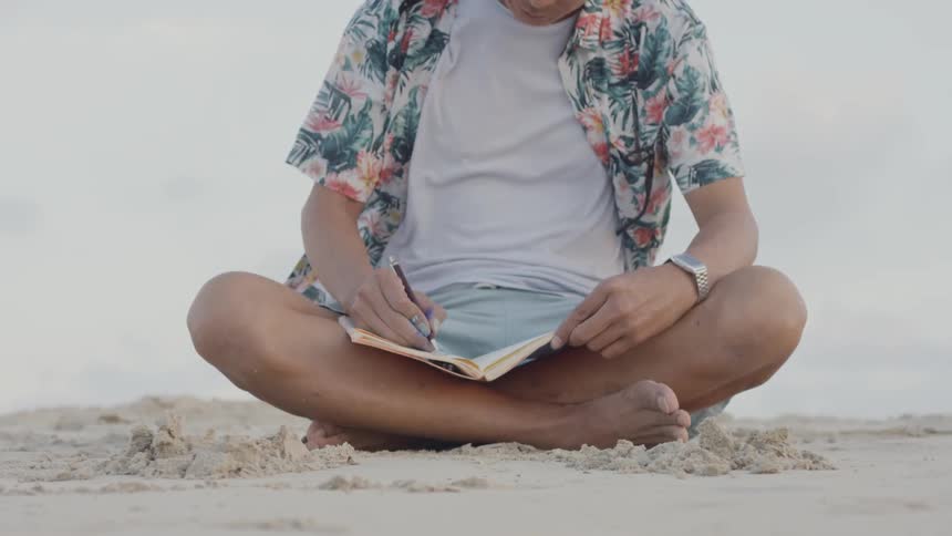 Person sits in the sand writing in a small book