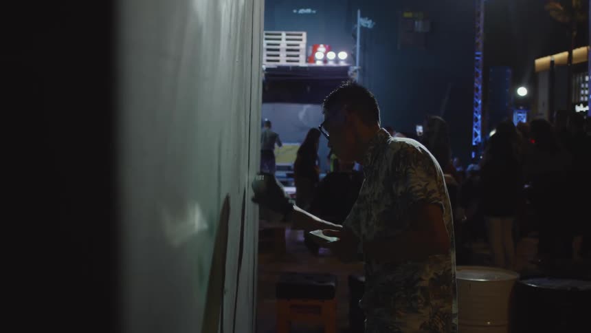 A man is spray painting a wall inside in a club at night