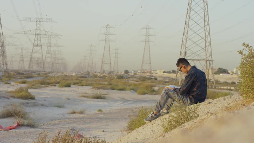 Man sits on a small sandy hill near many telephone poles