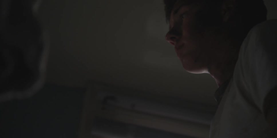 A white male teenager stands inside a dark room