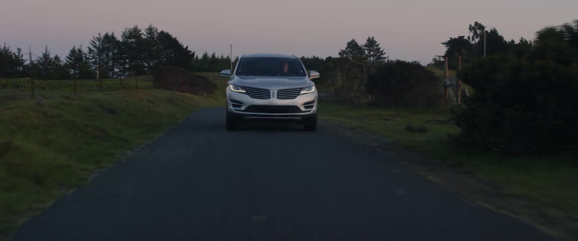 Silver car travels down a country road next to trees and fields