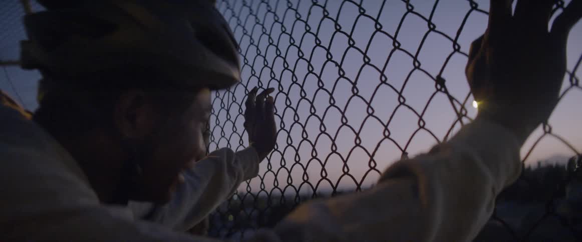 A man is breathing heavily as he leans against a fence on a bridge at dusk