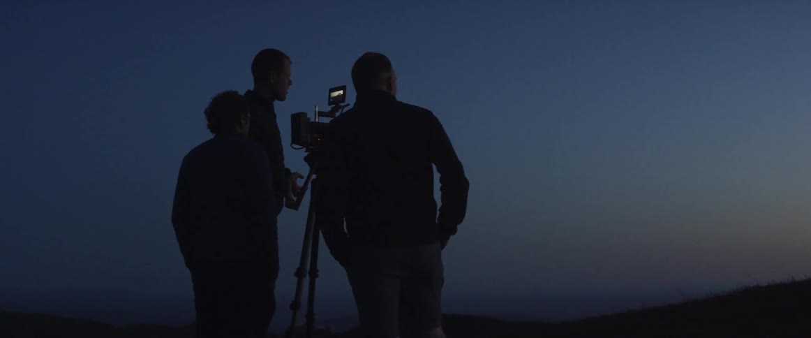 Three men consult as they set up a camera shot of a vehicle at dusk