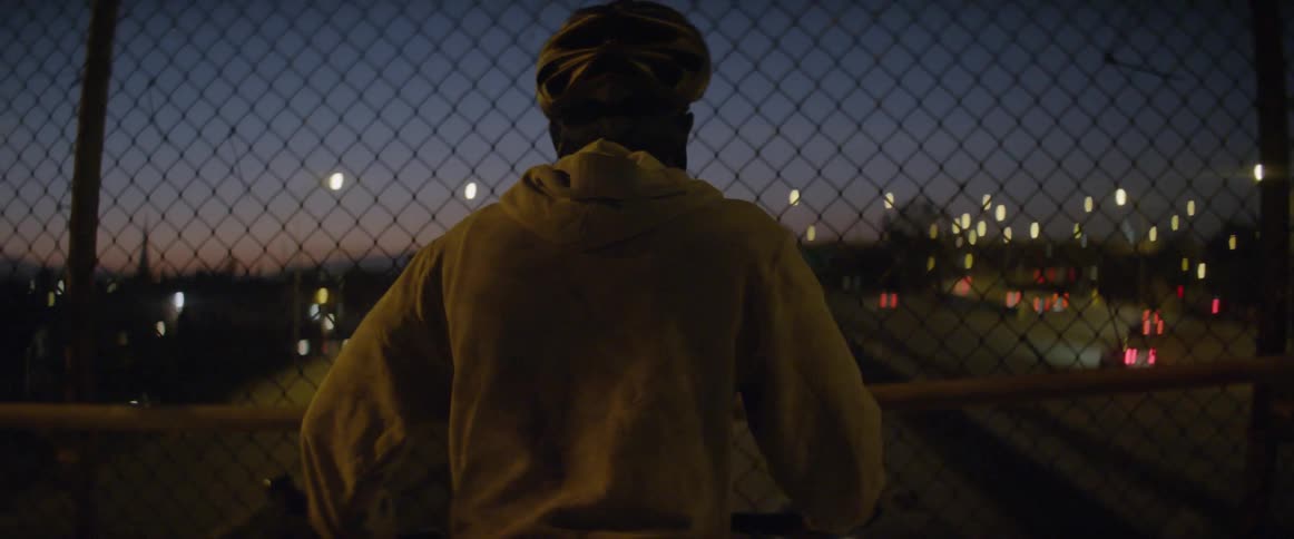 A man watches cars from a highway overpass at dusk