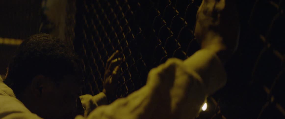A man puts his hands on a chain link fence at night