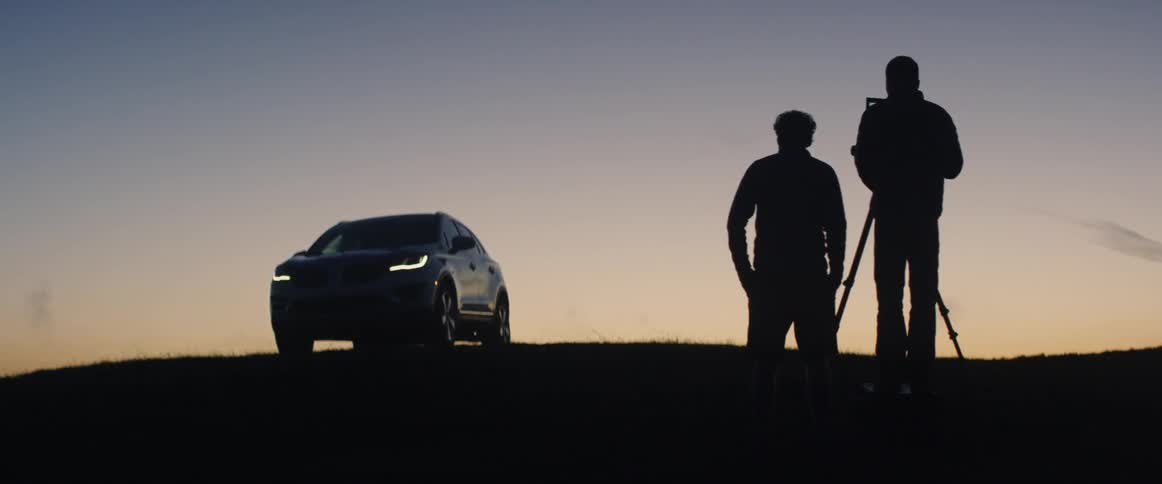 The people on the hill are photographing a vehicle at sunset