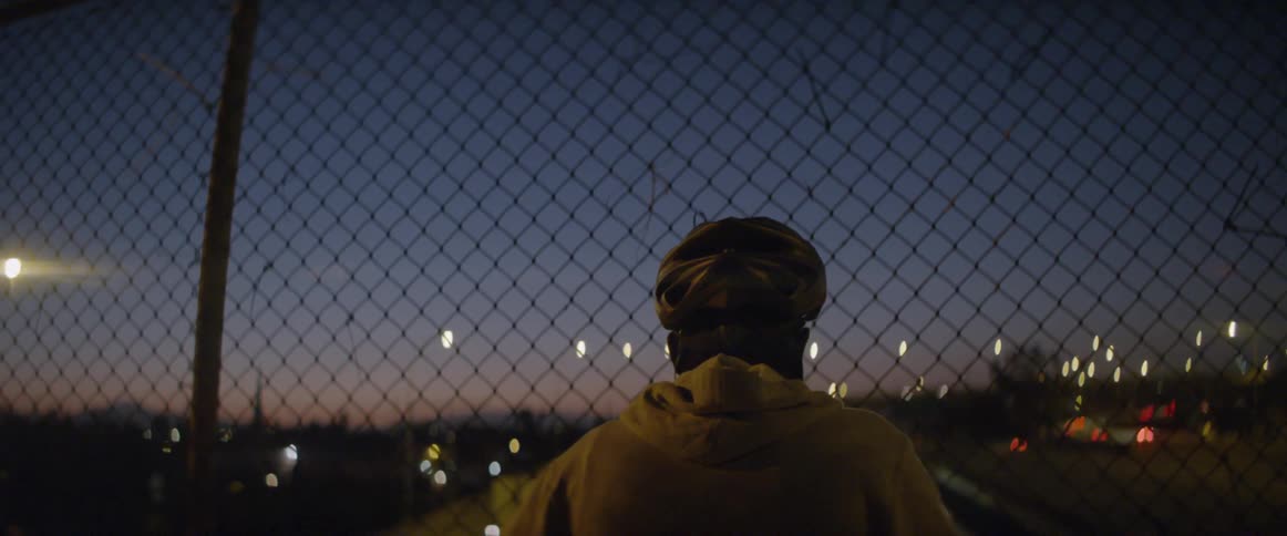 A man looks through a chain link fence overlooking a highway