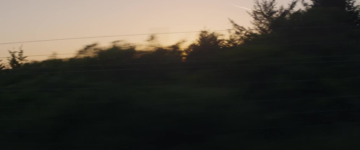 An airplane is leaving a vapor trail in the sky over a rural road at dusk