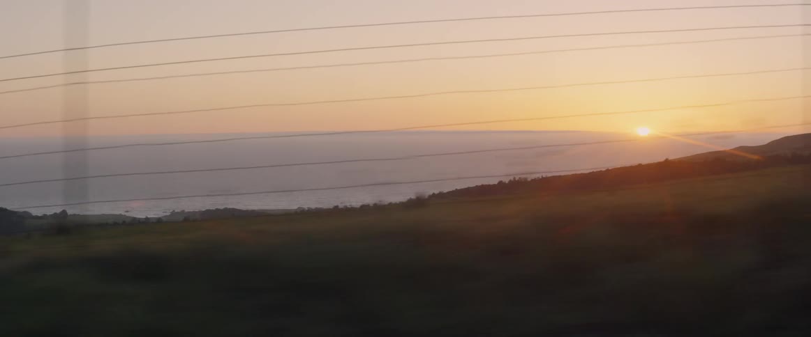 The sun is setting by the water down the hill