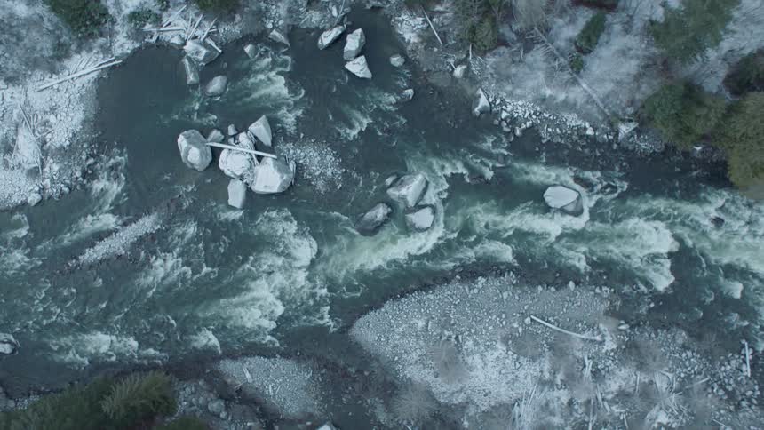 Birds eye view flying upstream above icy river rapids