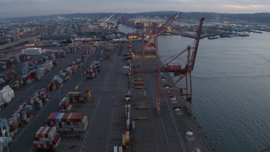 Seaport shipping containers stacked behind cranes on a dock