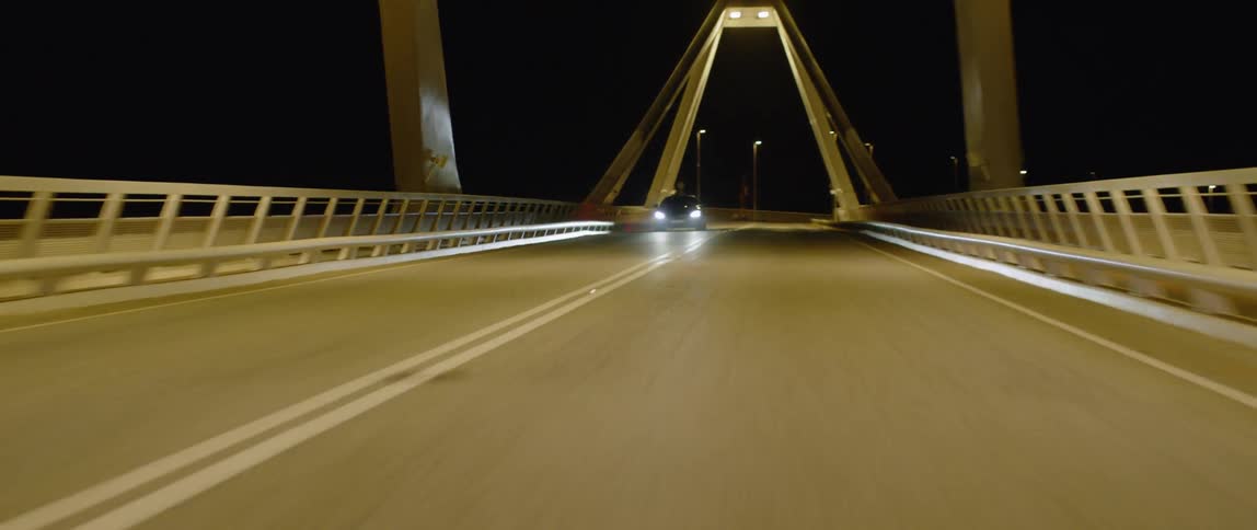 A car drives over a city bridge at night