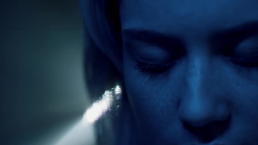 A woman stands in a dark room with her eyes closed