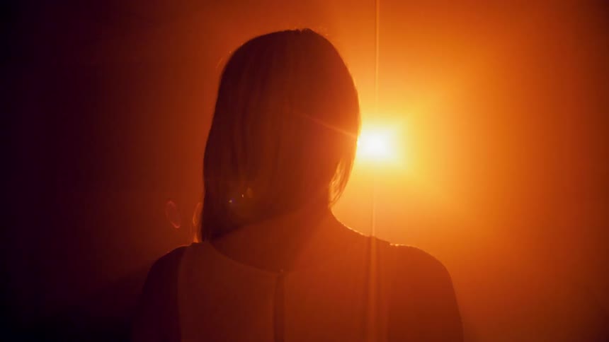 A woman stands in front of a bright light